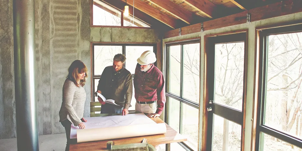 Builder and couple discussing custom home site plan at a design table in Western Colorado